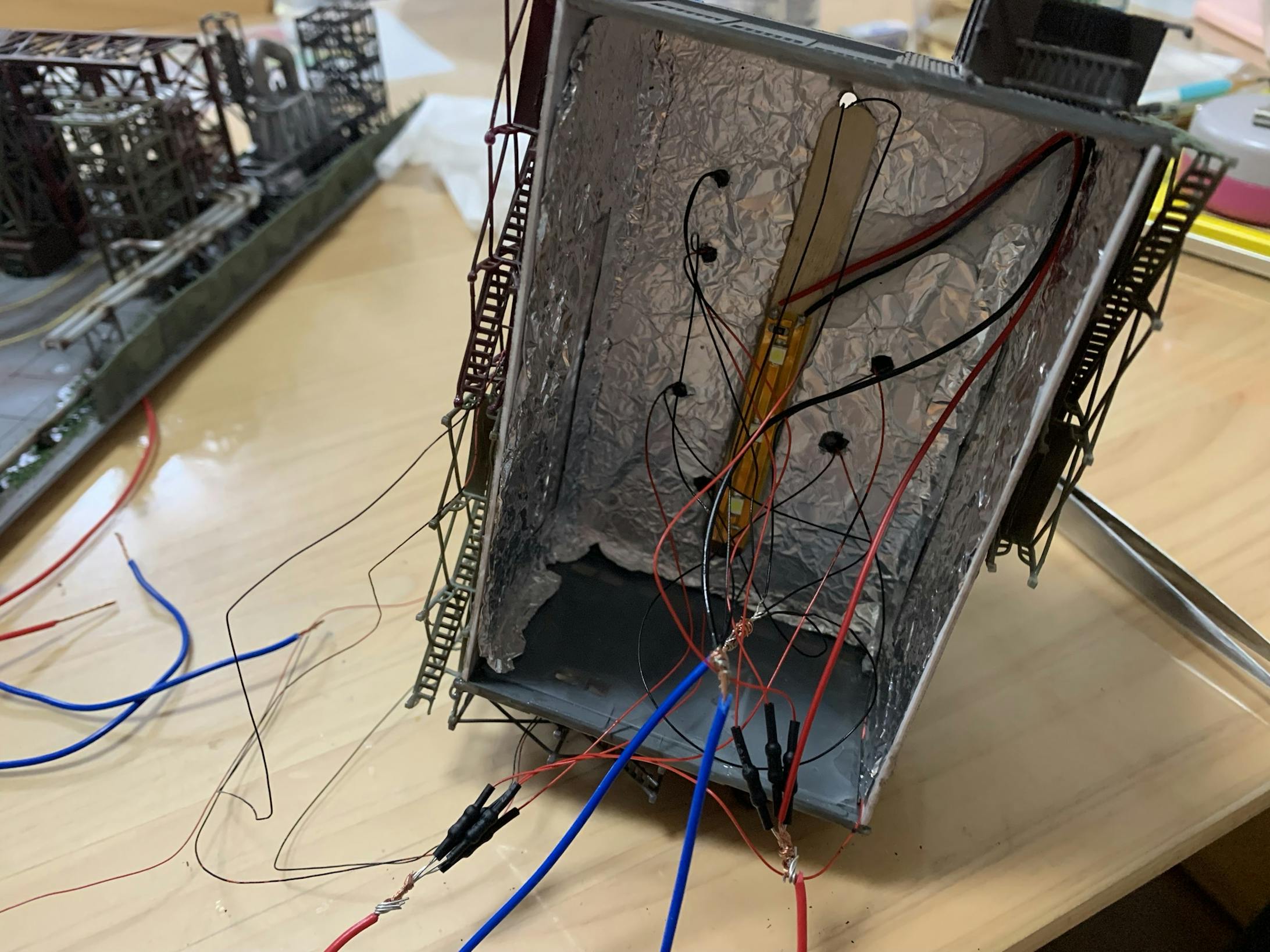 工場の壁から光が漏れて不自然にならないようにアルミホイルに木工ボンドをつけて固定しました。配線類は、取り付け位置がそれぞれ違うので、配線を束ねた時の長さも違います。なるべく同じ長さになる束をいくつか分けることにしました。2年前の作製当時、電気の知識がないため、LEDがどのくらいの電圧と電流でいくつまで点灯できるか分からなかったし、「スプリッターケーブルの一つは4つのLEDしかつかないのかなあ、5.6個もLEDを一つの足につけて、点灯しなくなるとやだなぁ、だから4LED×8本は32個かなあ」とかモヤモヤ考えながら作りました。そんな感じで分からないなりに調べて、色々実験して、かなり遠回りをしてきました。 工場の壁から光が漏れて不自然にならないようにアルミホイルに木工ボンドをつけて固定しました。配線類は、取り付け位置がそれぞれ違うので、配線を束ねた時の長さも違います。なるべく同じ長さになる束をいくつか分けることにしました。2年前の作製当時、電気の知識がないため、LEDがどのくらいの電圧と電流でいくつまで点灯できるか分からなかったし、「スプリッターケーブルの一つは4つのLEDしかつかないのかなあ、5.6個もLEDを一つの足につけて、点灯しなくなるとやだなぁ、だから4LED×8本は32個かなあ」とかモヤモヤ考えながら作りました。そんな感じで分からないなりに調べて、色々実験して、かなり遠回りをしてきました。