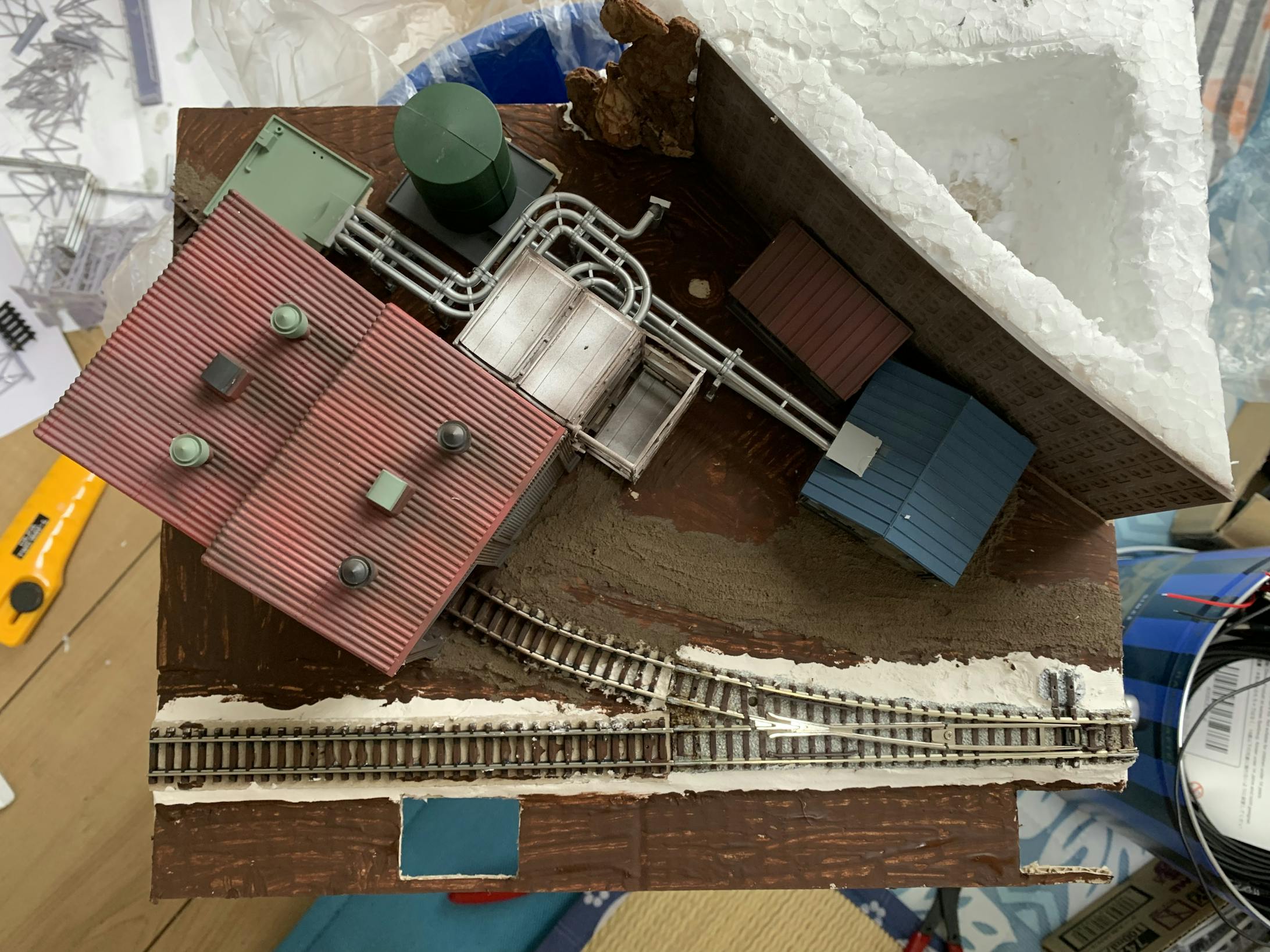 イメージに合わせて仮置きしてみました。TOMIXで作った専用線は、線路の素材のままだとおもちゃ感が出てしまう為、線路脇を石膏粘土で覆い、周りの地面と馴染ませました。この後、この石膏粘土にグレイで着色し、バラストを撒き、ボンド水で固着させ、さらに線路を使い古されたように錆び色を塗装していきます。 イメージに合わせて仮置きしてみました。TOMIXで作った専用線は、線路の素材のままだとおもちゃ感が出てしまう為、線路脇を石膏粘土で覆い、周りの地面と馴染ませました。この後、この石膏粘土にグレイで着色し、バラストを撒き、ボンド水で固着させ、さらに線路を使い古されたように錆び色を塗装していきます。